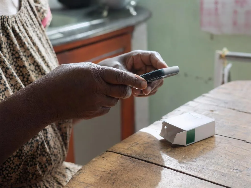 Des mains tiennent un téléphone au-dessus d'une boîte de médicament posée sur une table en bois.